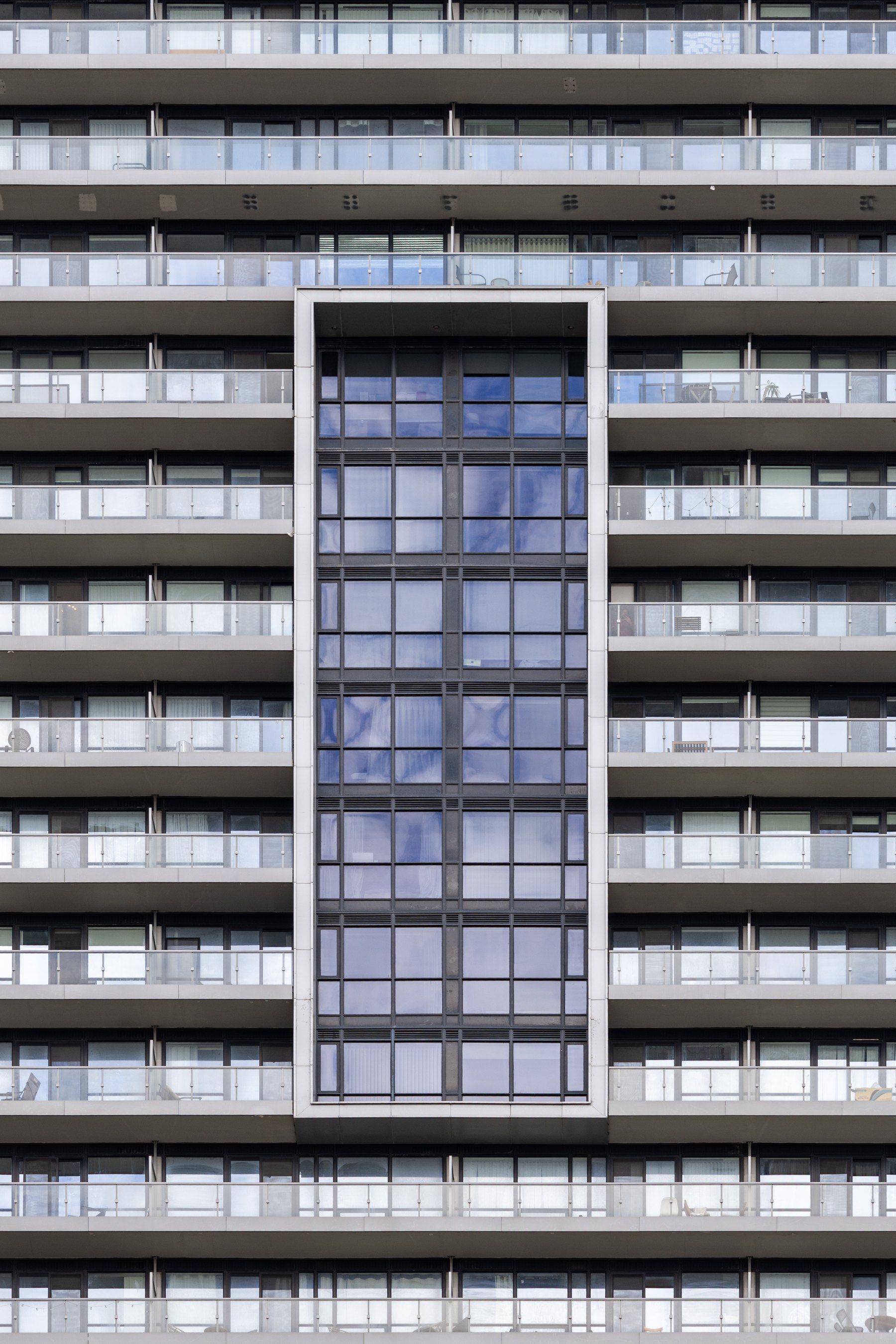 Repeating balconies and a tall glazed stairwell on a modern apartment tower