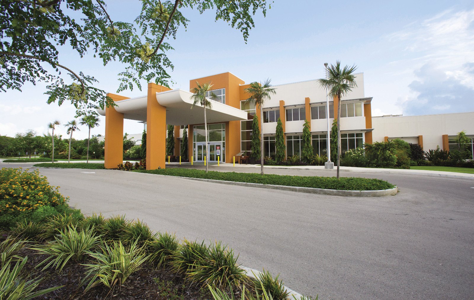 Modern two-storey medical building with orange columns, glass entrance and tropical landscaping