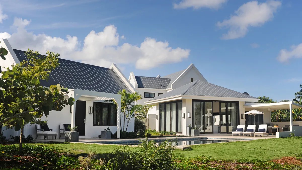 White modern villa with metal roof, palms and a swimming pool under blue sky