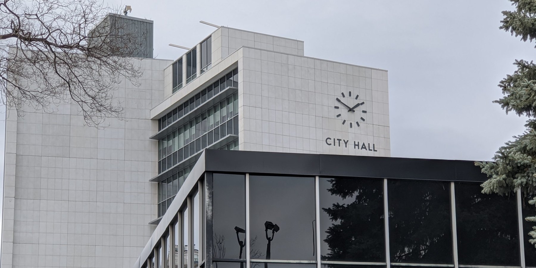 Pale stone civic building with a minimalist clock and lettering above a glass entrance