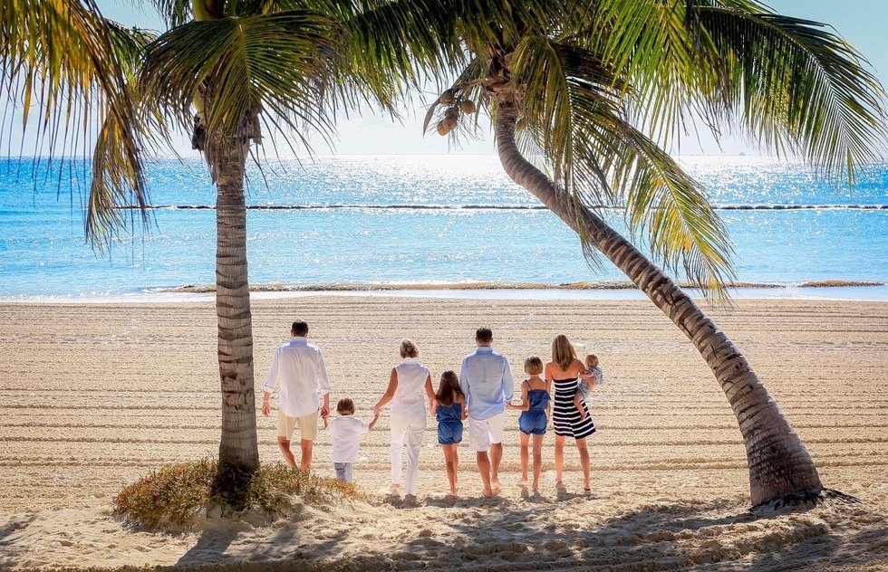 Multigenerational family stands beneath leaning palm trees looking out at a calm turquoise sea