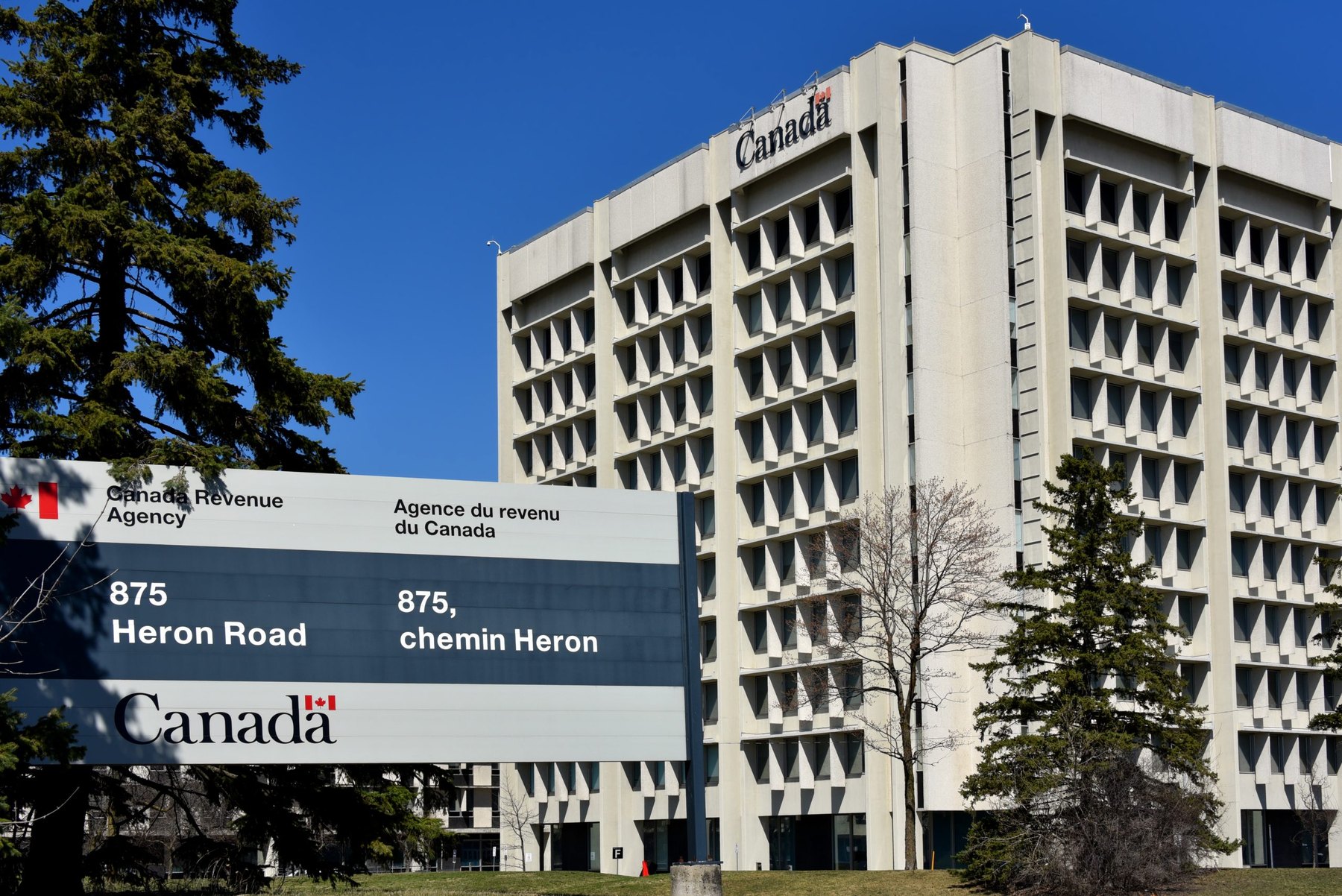 Modernist government office tower behind a large bilingual sign for a national revenue agency
