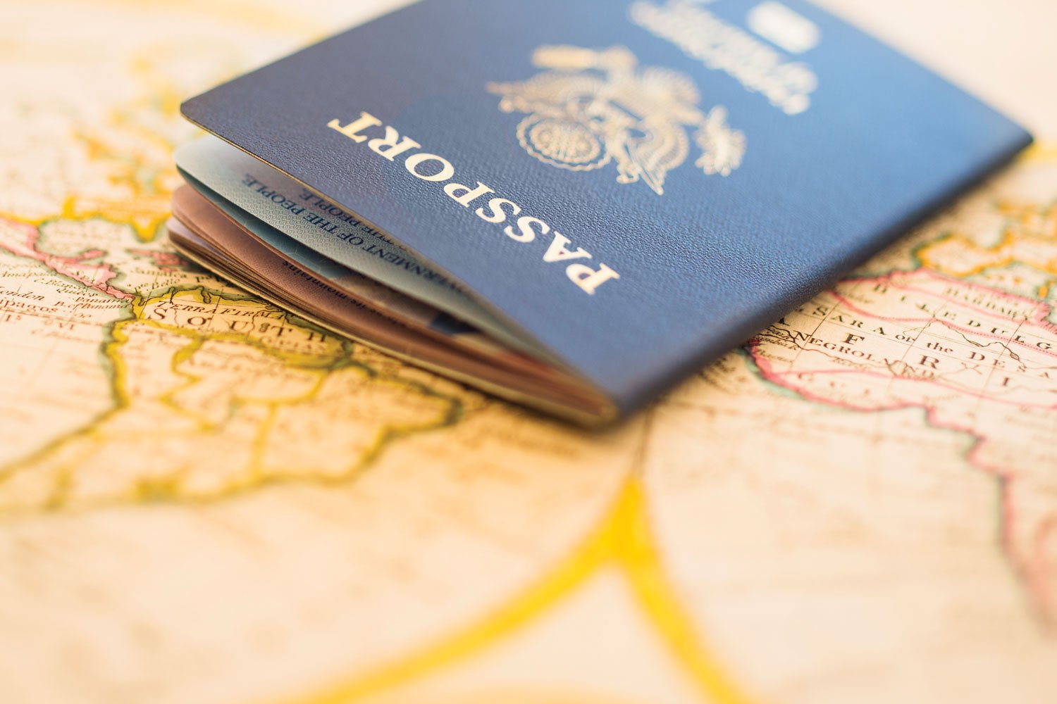 A navy passport lies half open on a hand-coloured antique map, shallow focus