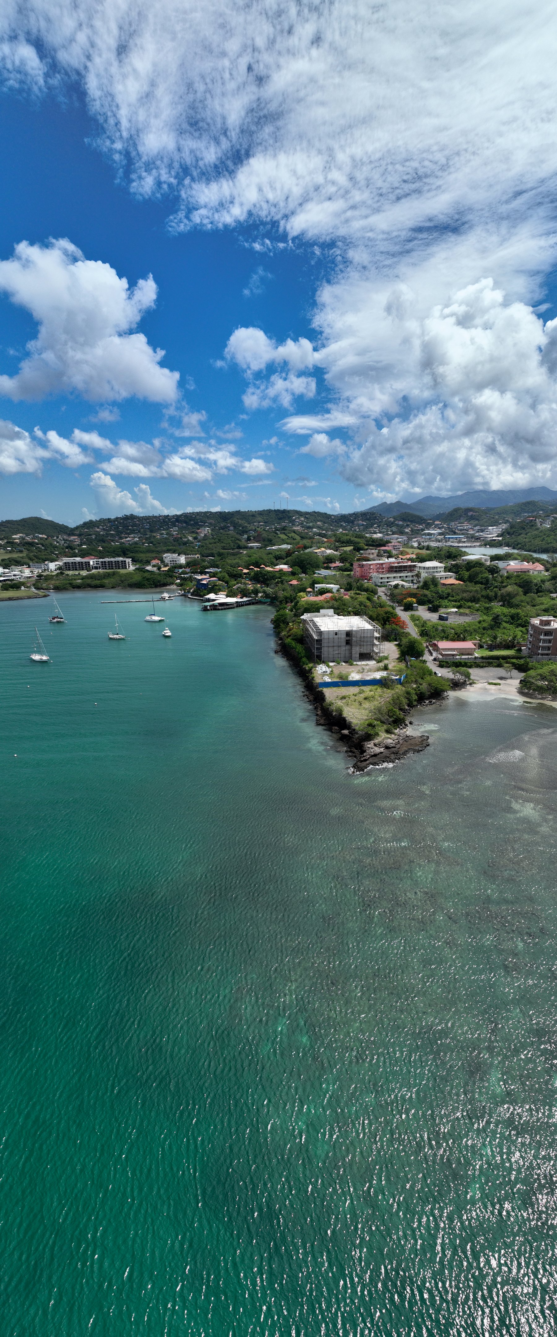 Vertical aerial of True Blue Bay's turquoise water, moored yachts and the development site