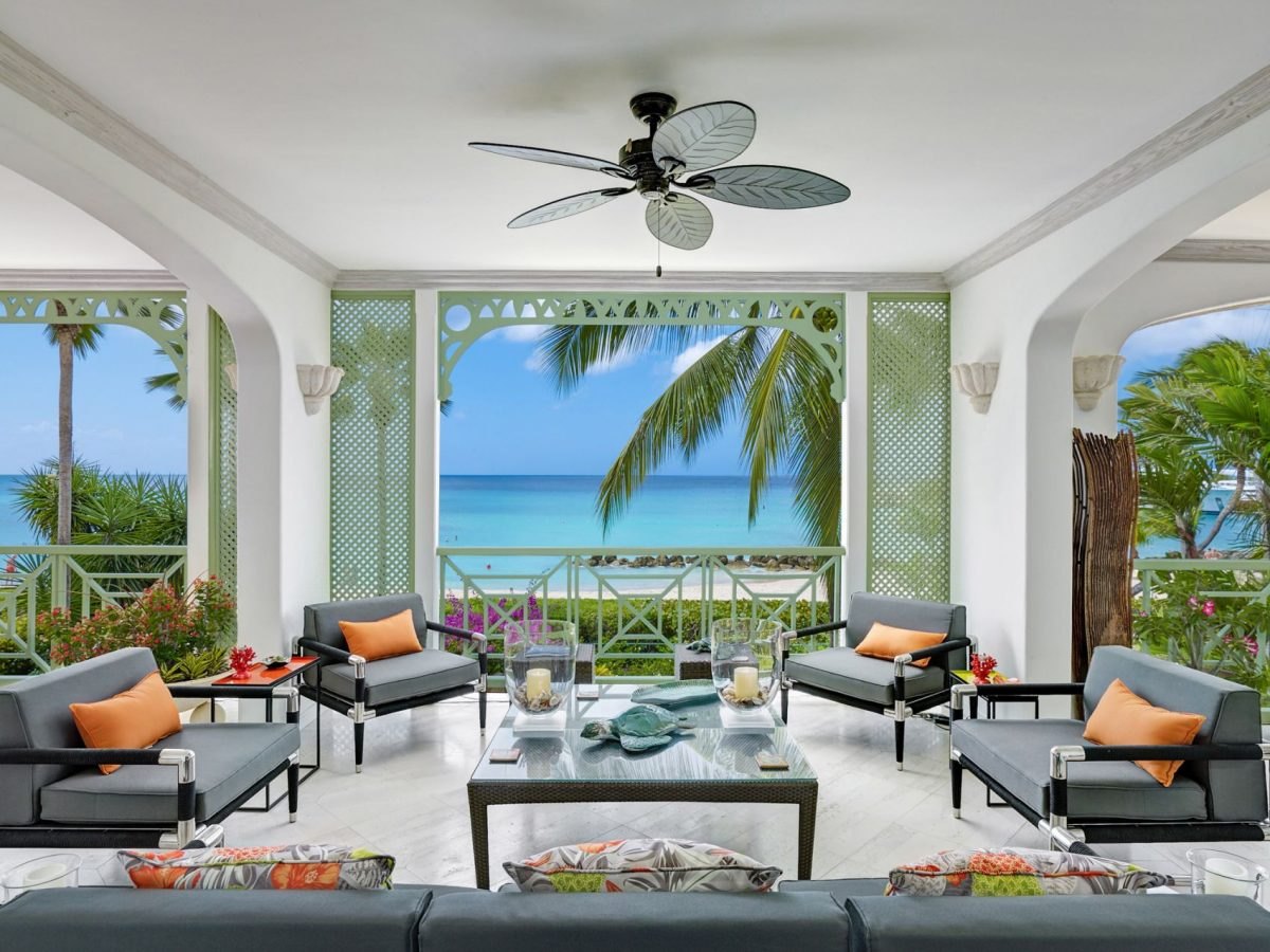 Furnished open-air veranda with ceiling fan looking out through arches to a turquoise sea
