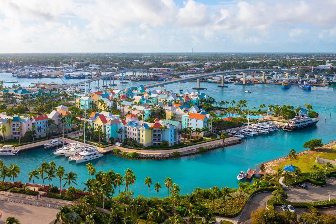 Aerial view of pastel townhouses beside a marina with yachts, catamarans and a road bridge