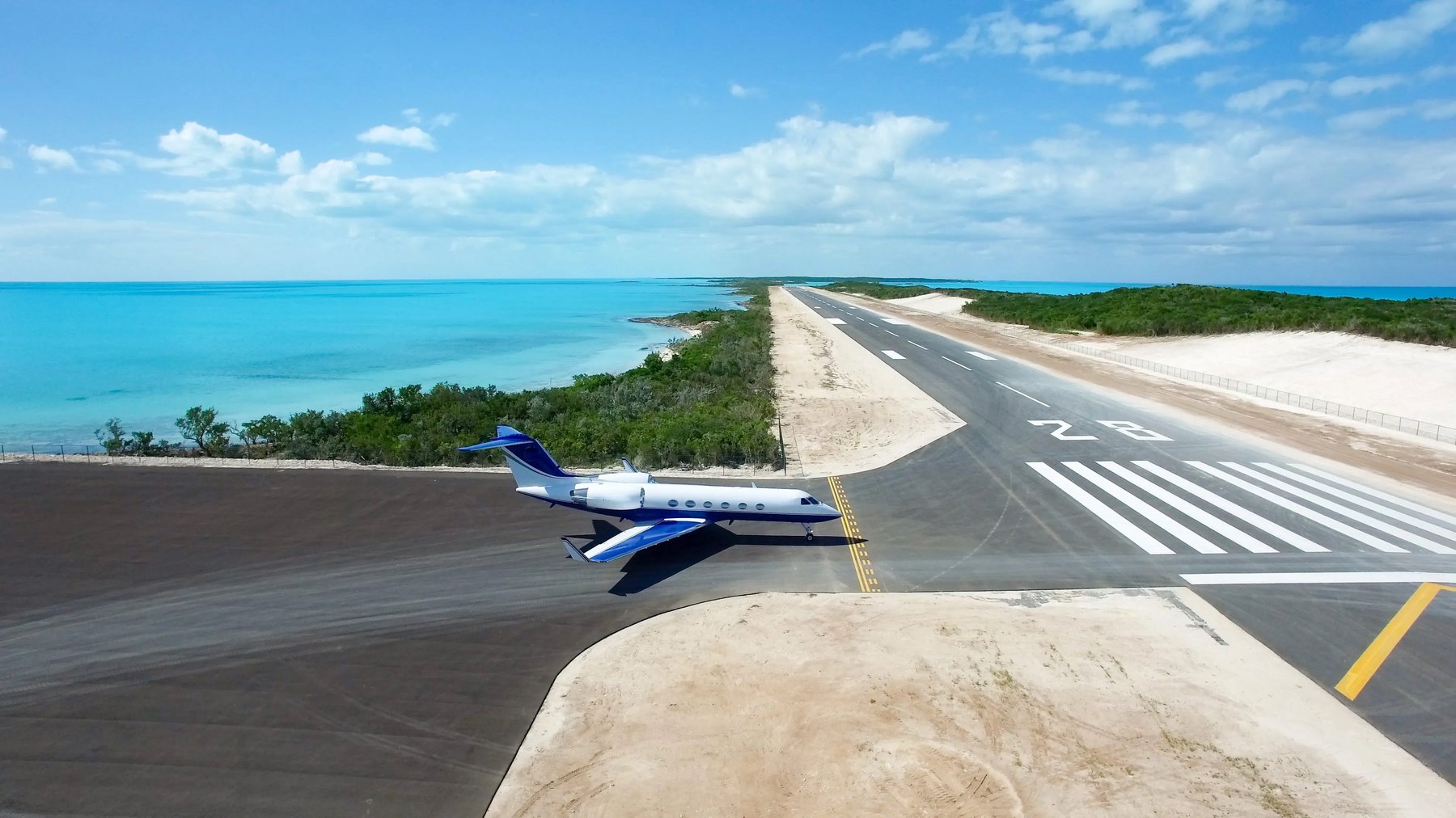 Private jet holding at the end of a short island runway, turquoise shallows on both sides