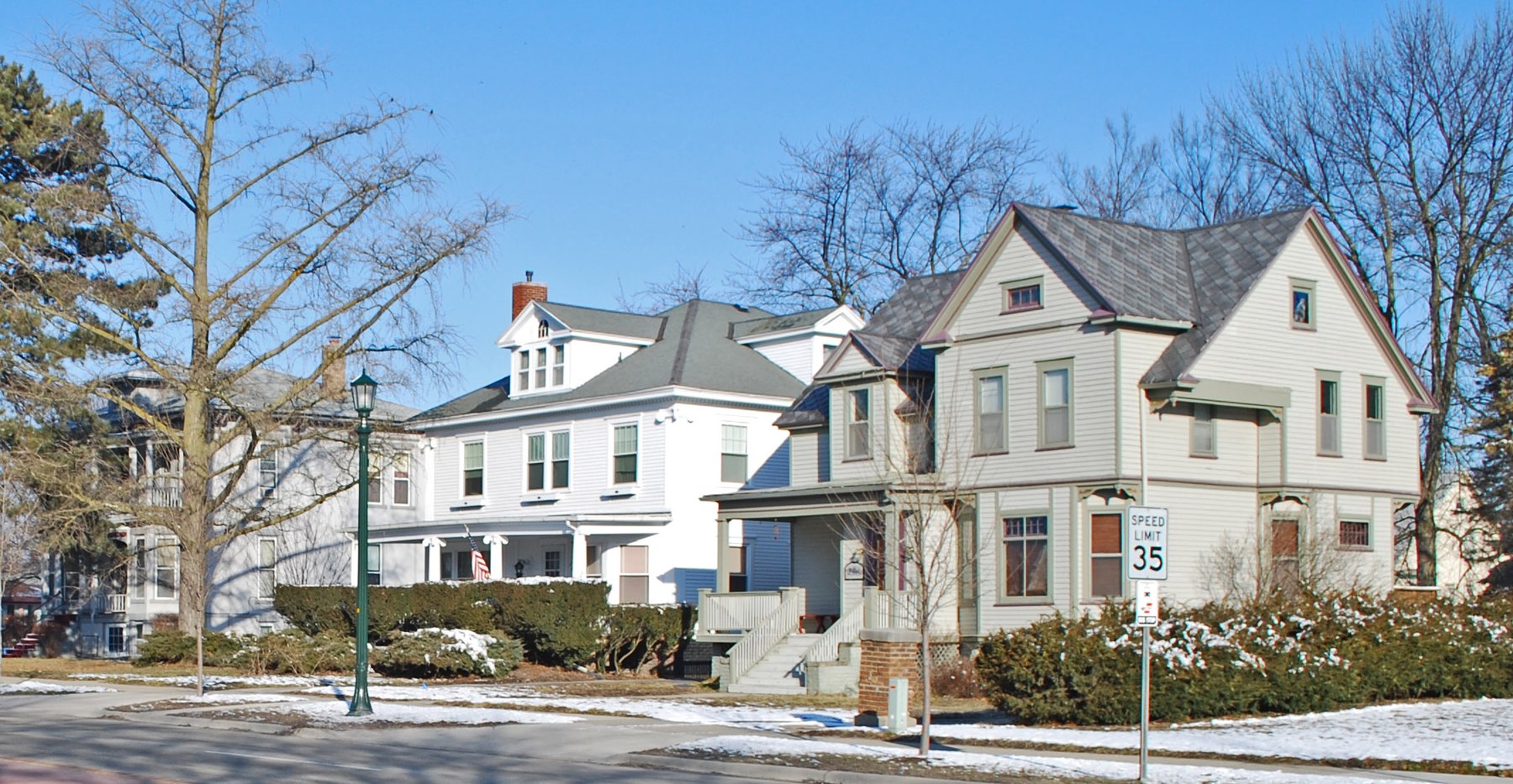 Two large Victorian clapboard houses on a quiet residential street with light snow