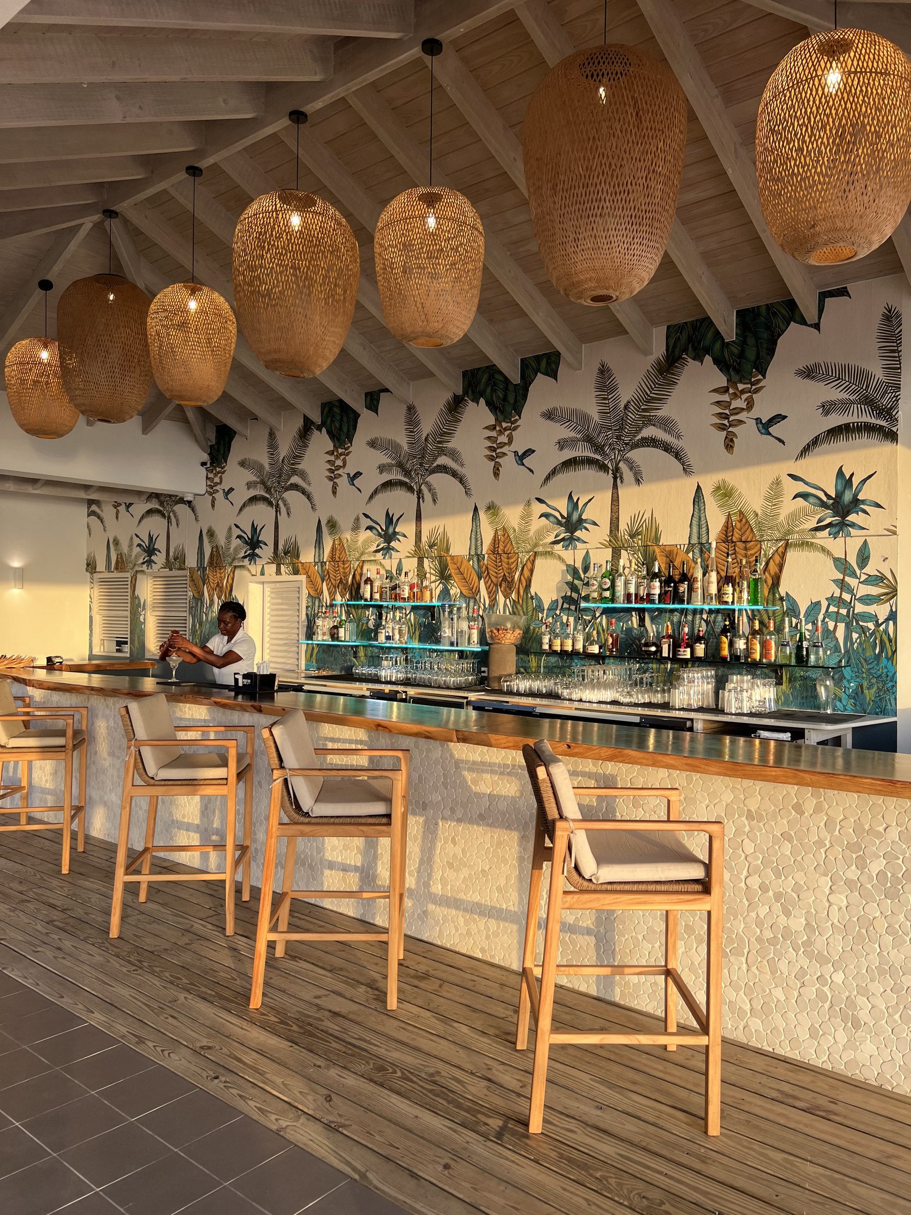 Empty resort bar with rattan pendant lights, timber stools and a painted tropical mural