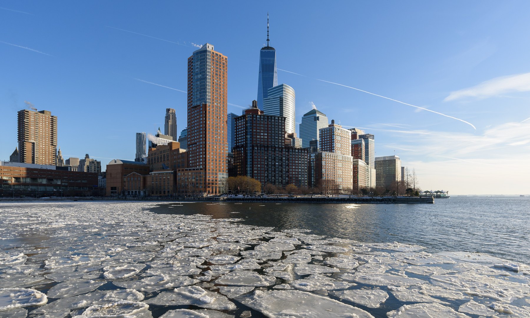 Broken ice floes on a river before a sunlit downtown waterfront skyline in winter