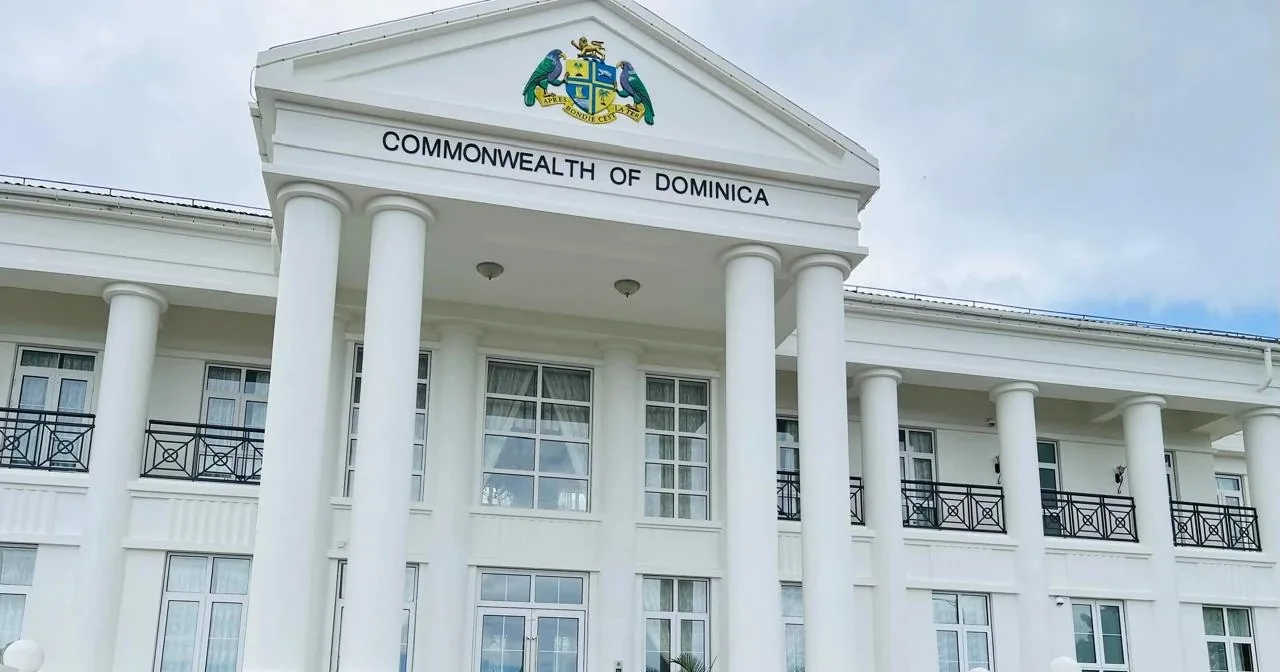 White neoclassical government building in Dominica, its columned portico pediment lettered Commonwealth of Dominica beneath the national coat of arms