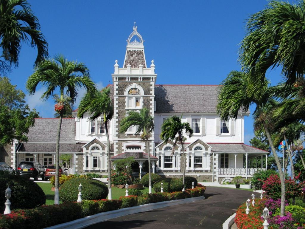 White and stone colonial government house with clock tower, framed by royal palms
