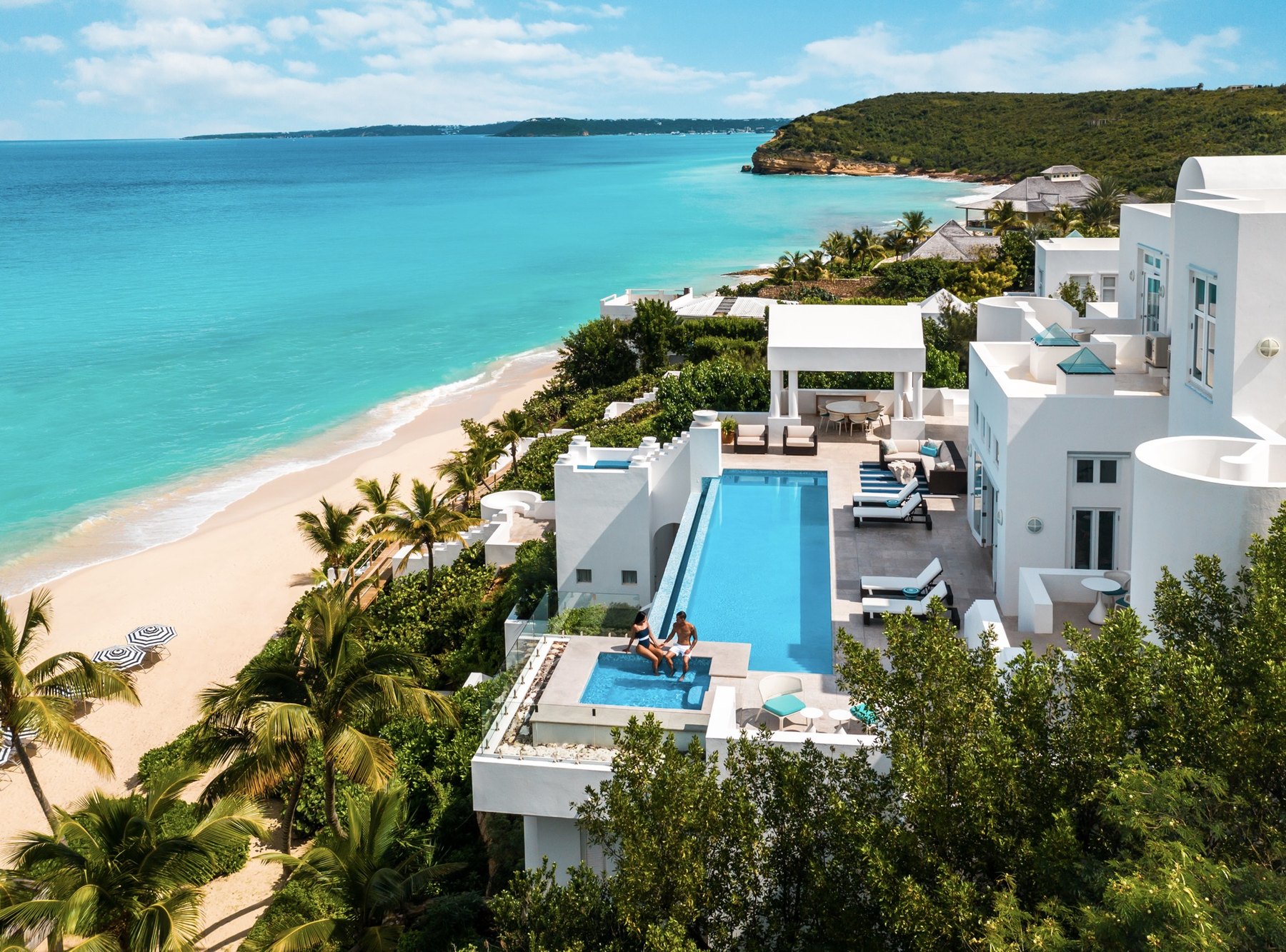 Whitewashed Anguilla villa terrace with infinity pool overlooking a curving turquoise bay and palm-fringed beach