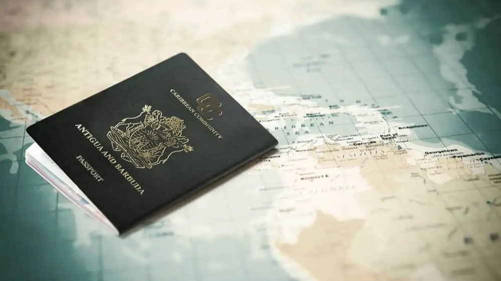 An Antigua and Barbuda passport with gold Caribbean Community lettering resting on a printed map of the Caribbean Sea