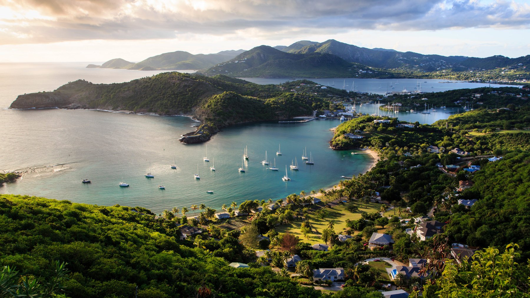 English Harbour and Falmouth Harbour on Antigua's south coast at golden hour, with yachts at anchor and hillside houses above