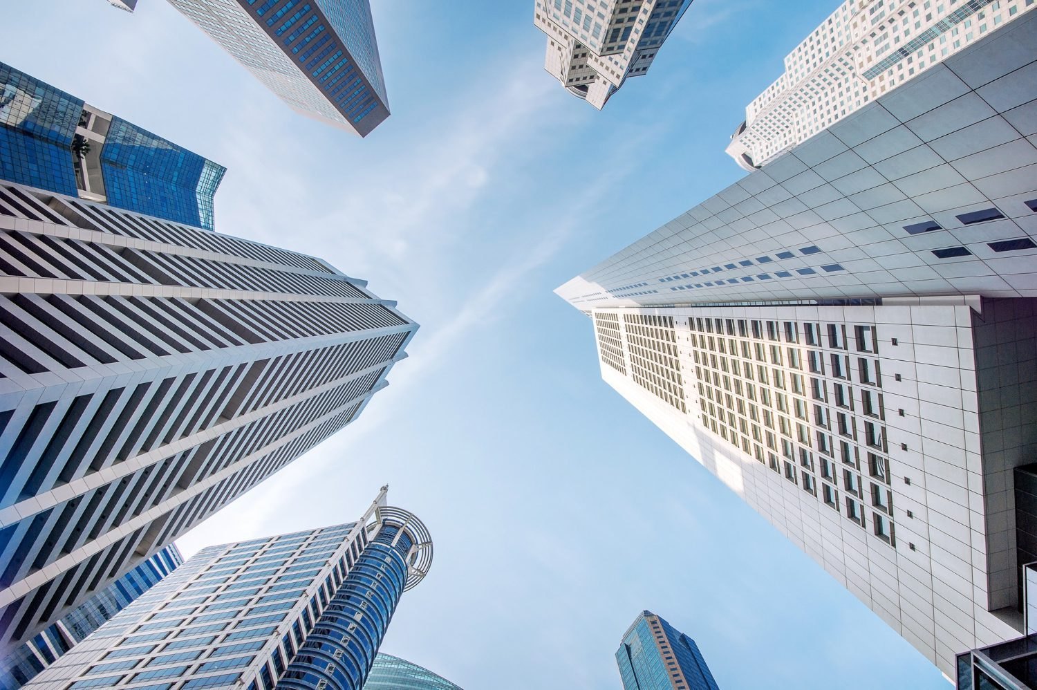 Upward view of glass and stone skyscrapers converging toward a clear blue sky