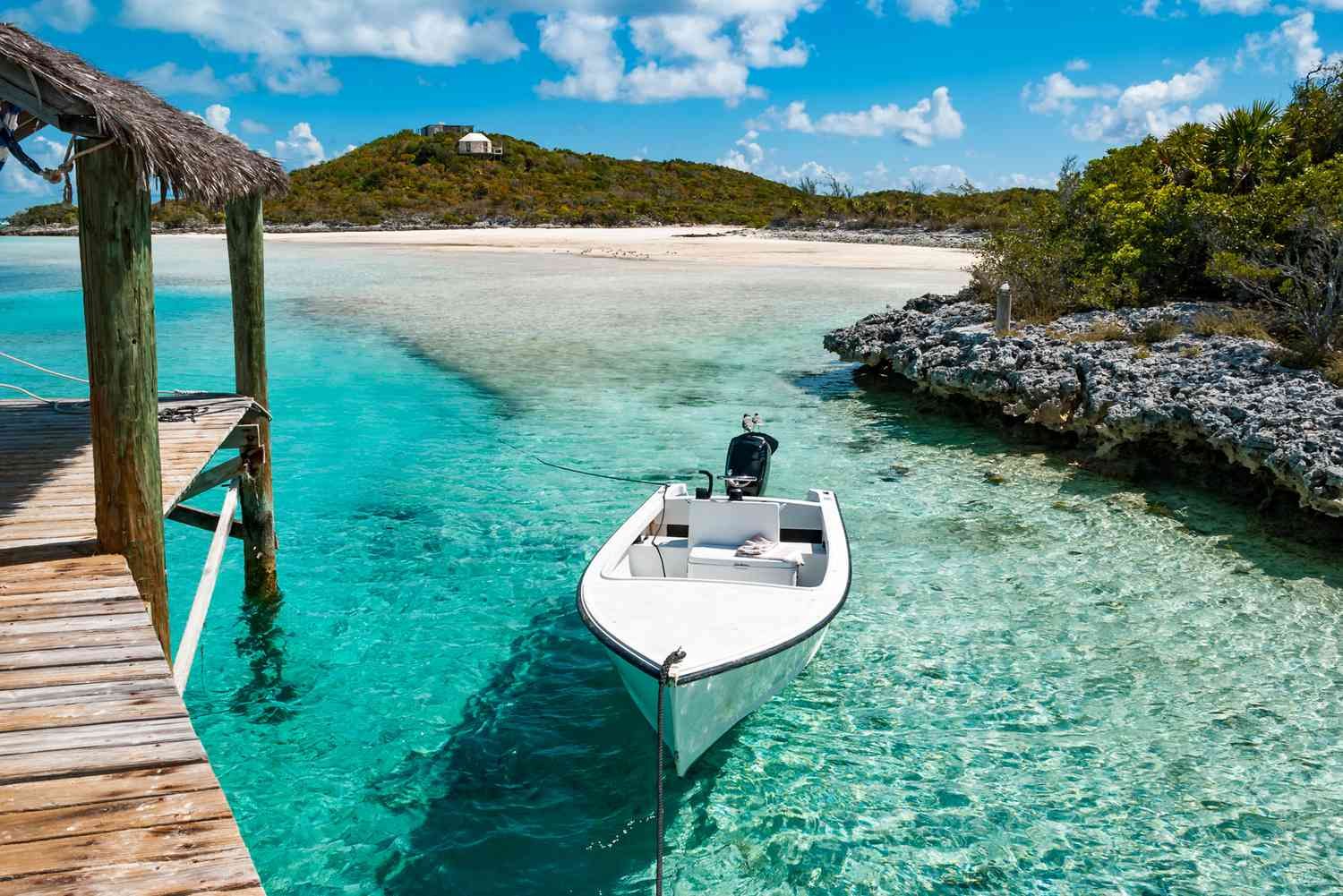 A small white skiff tied beside a weathered wooden dock in clear turquoise water