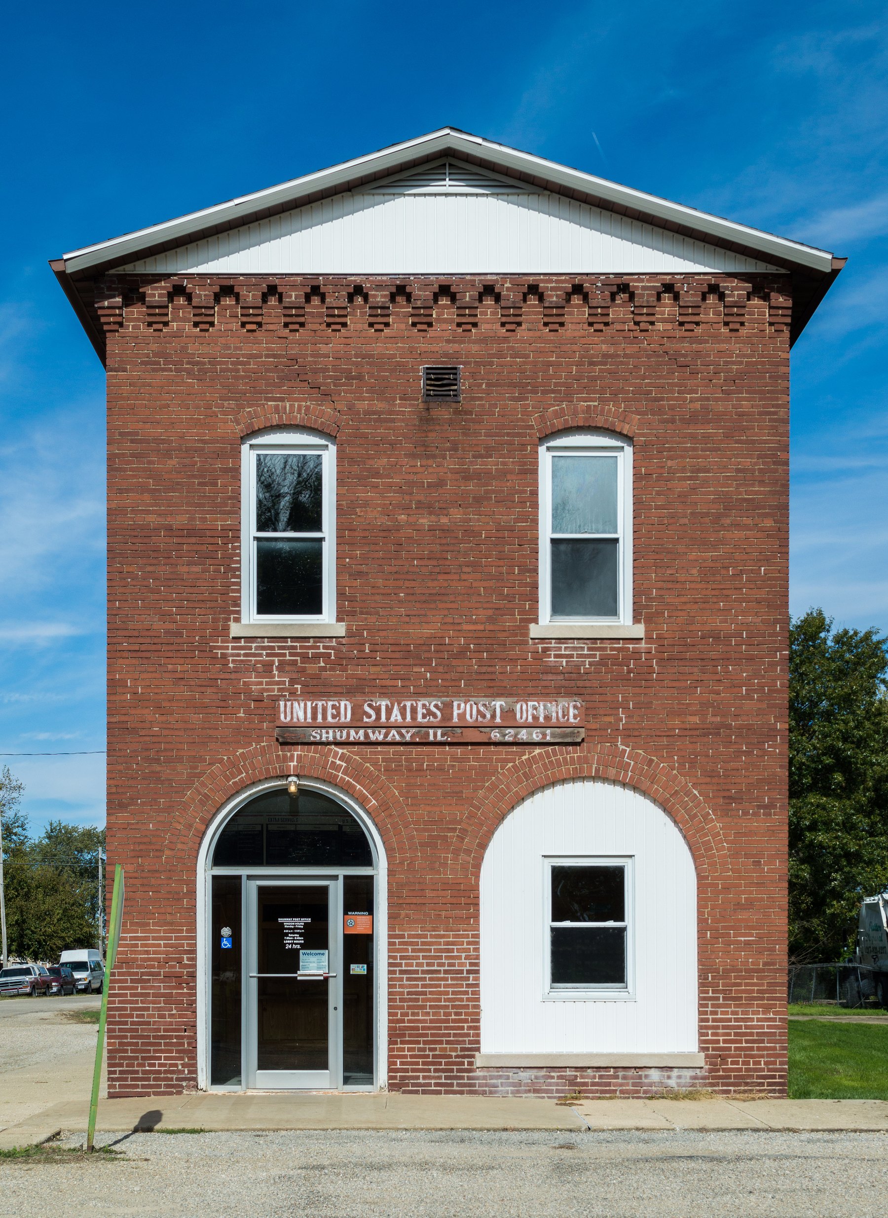 Two-storey red brick United States post office with arched doorway under blue sky