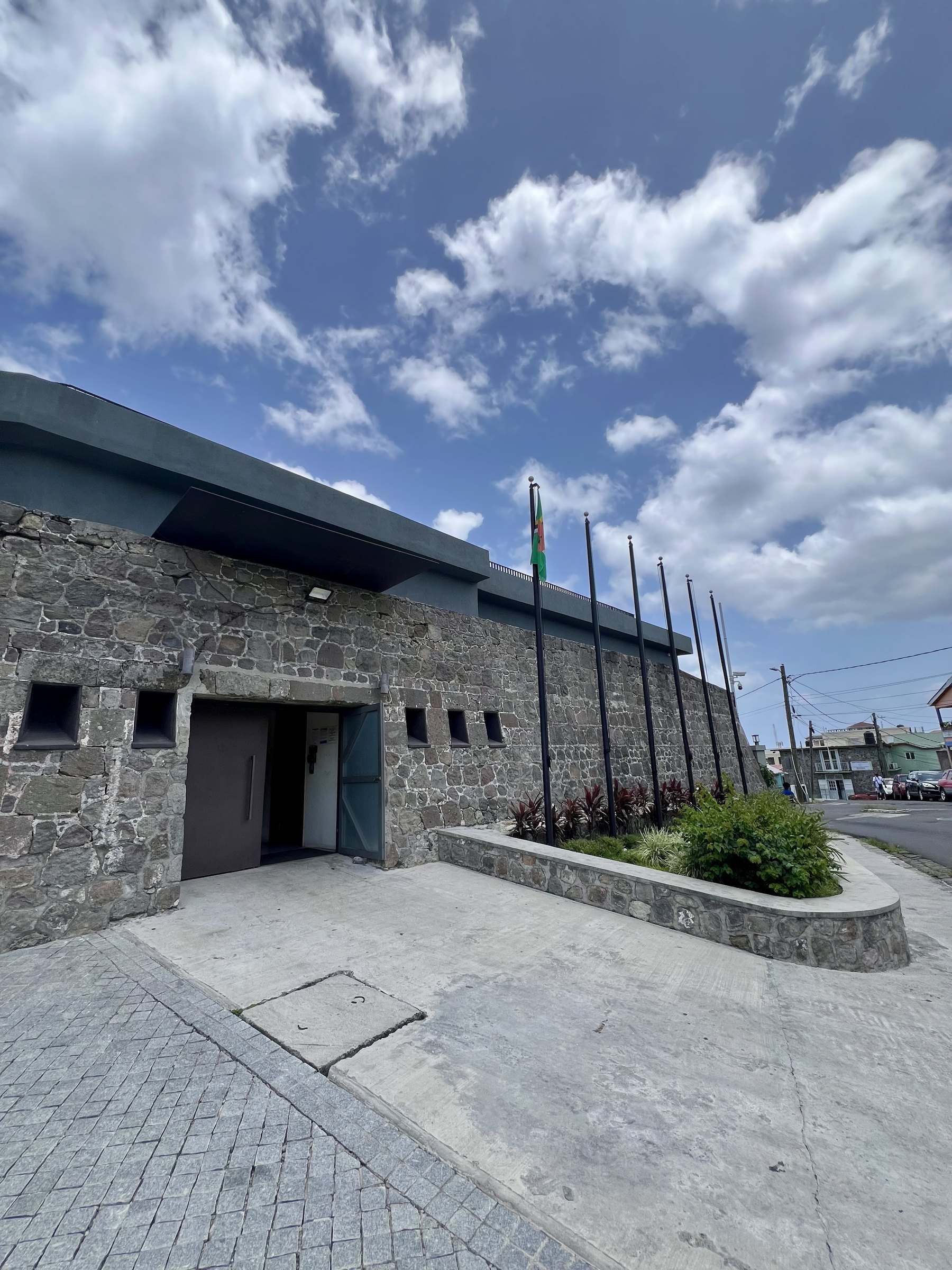 Stone fortress wall with a row of tall flagpoles and one flag flying.
