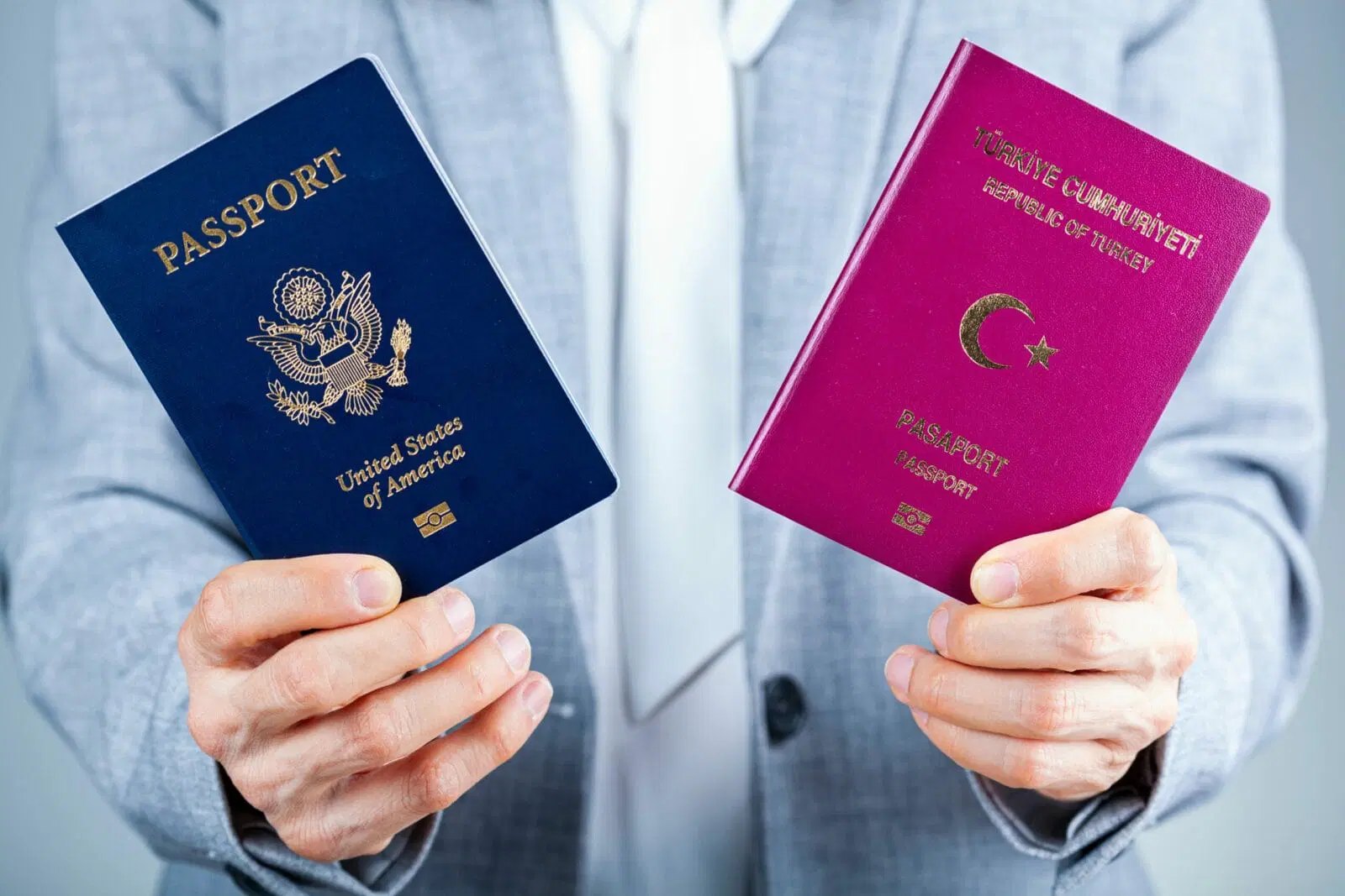 Person in a grey suit holding out two national passports, one navy one magenta