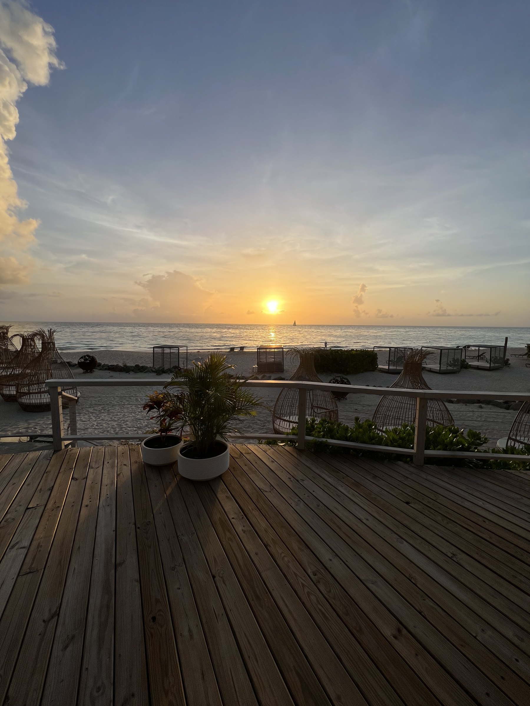 Sun setting over the sea seen from a timber deck above beach cabanas and loungers