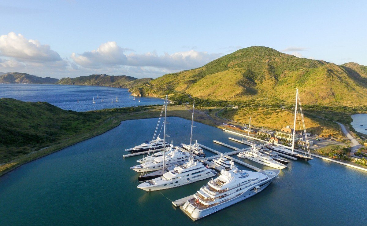 Aerial view of large motor yachts berthed side by side in a sheltered marina below green hills