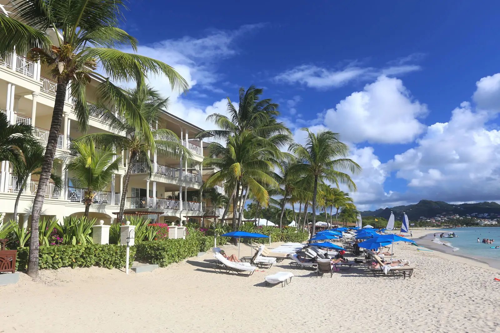 Beachfront residences at The Landings, St. Lucia, with palms, loungers and blue beach umbrellas
