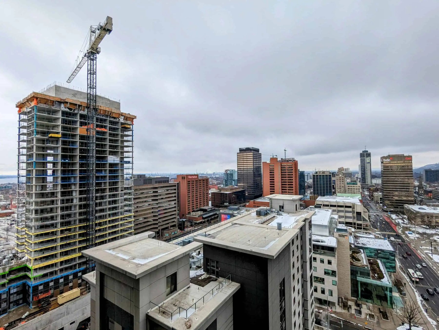 Tower crane atop a partly built high-rise overlooking a grey winter downtown skyline