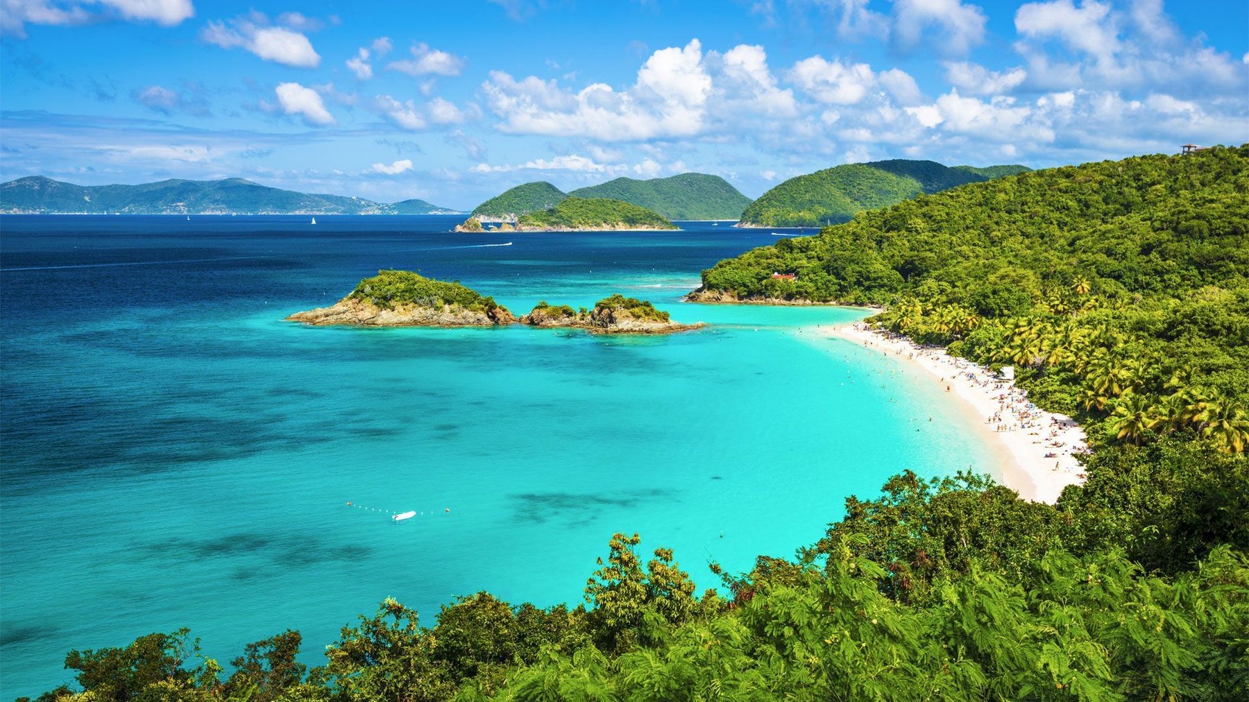 Elevated view of a turquoise bay with small wooded islets and a curving white beach