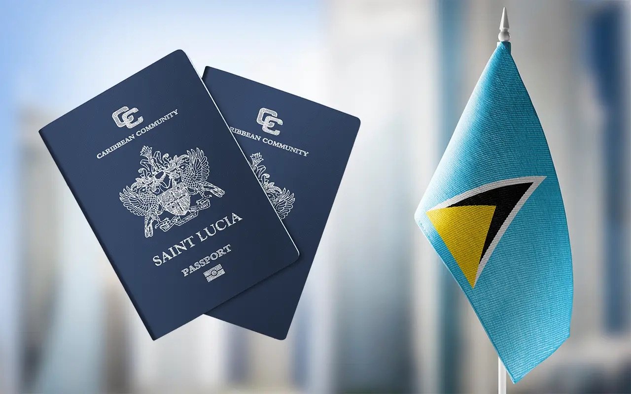 Two dark blue Caribbean Community passports beside a small desk flag, blurred buildings behind