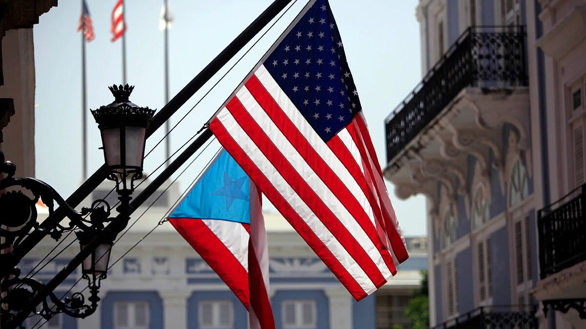 United States and Puerto Rican flags hang from a wrought-iron balcony on a colonial facade