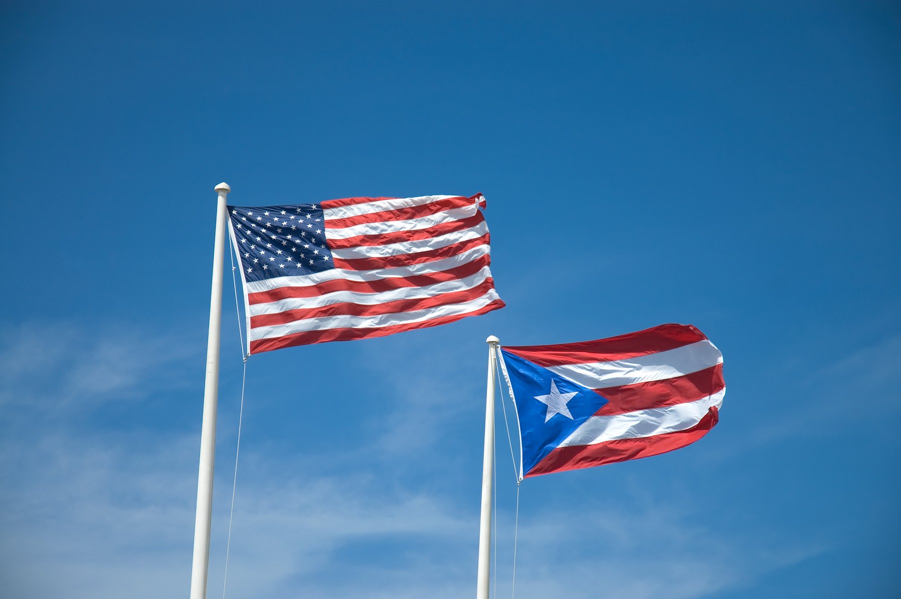 Two striped flags fly from white poles against a deep blue nearly cloudless sky
