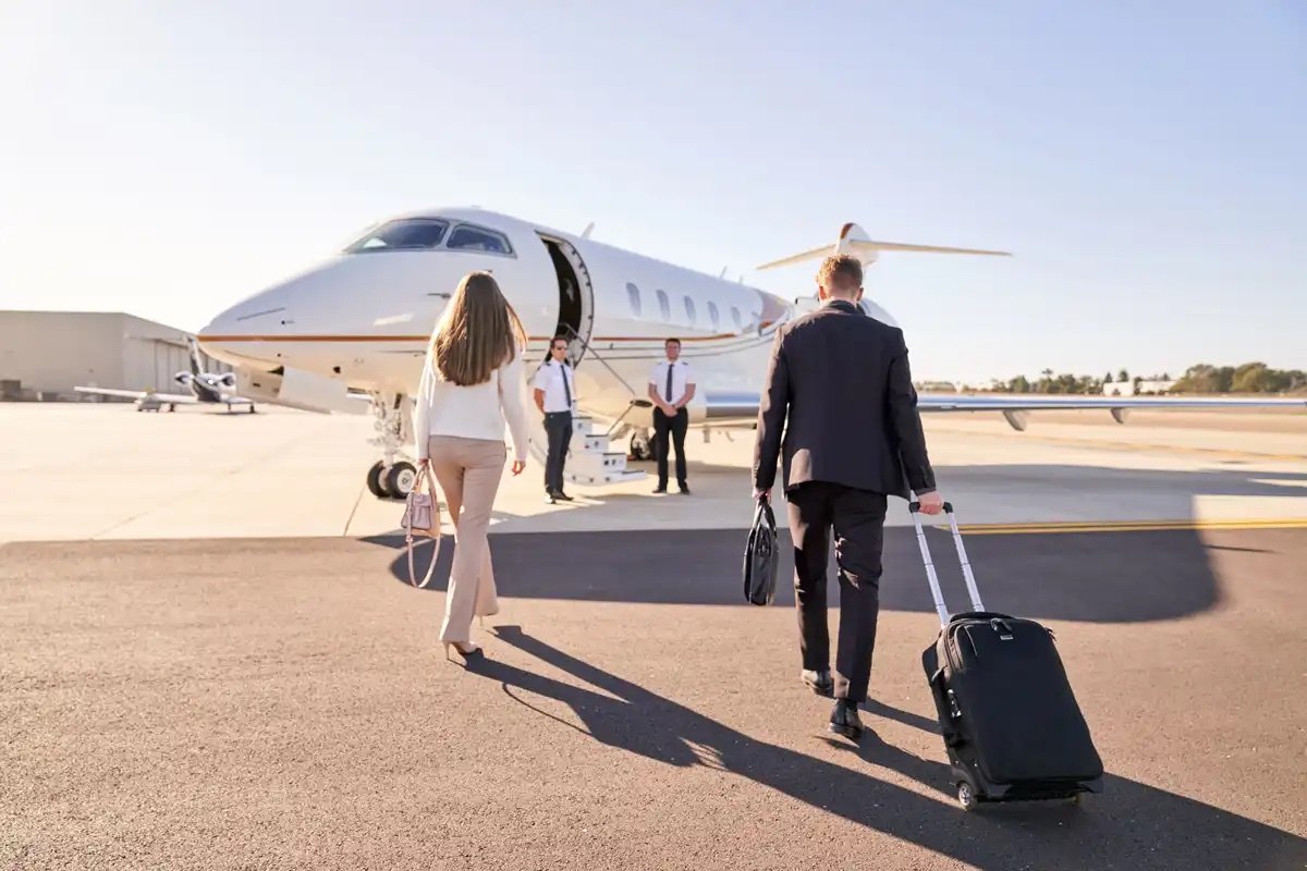 Two travellers with luggage walk toward a waiting private jet on sunlit tarmac