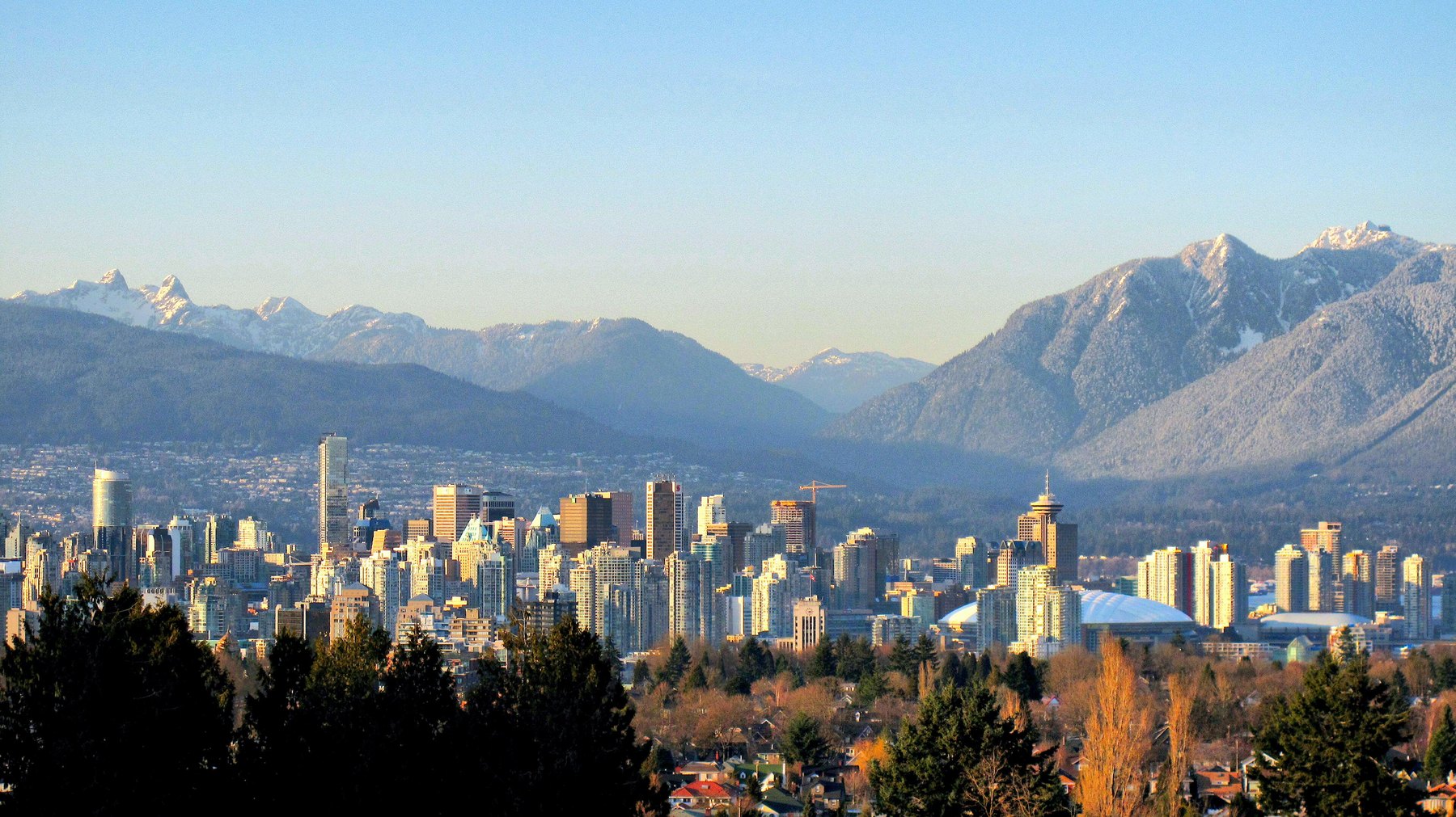 Vancouver's downtown skyline below snow-dusted coastal mountains in low winter light