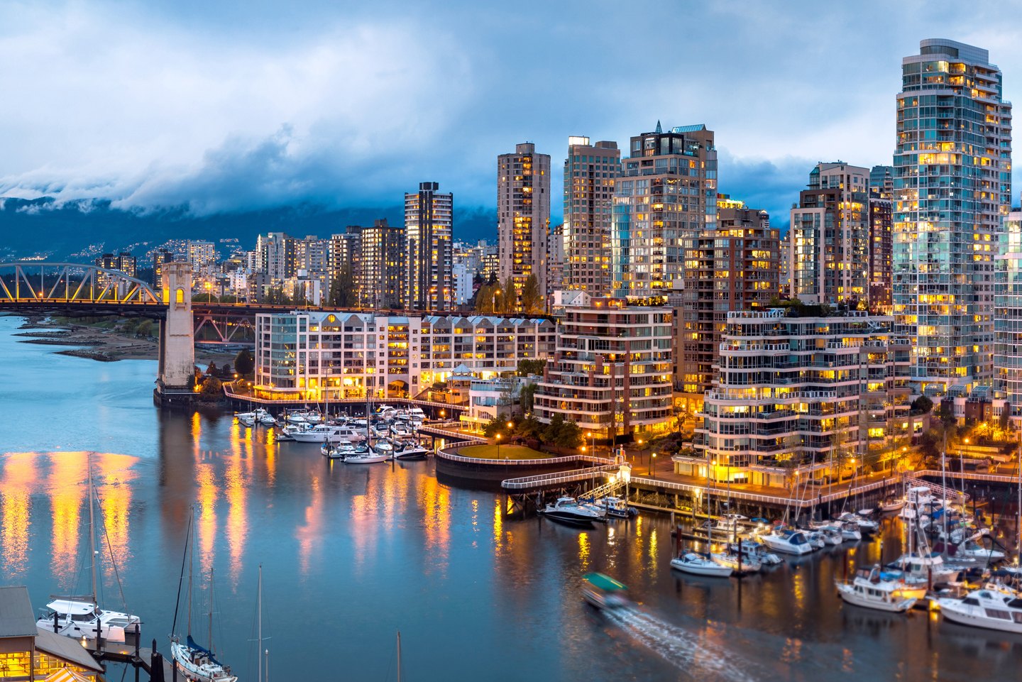 Glowing waterfront apartment towers above a marina full of moored yachts at blue hour