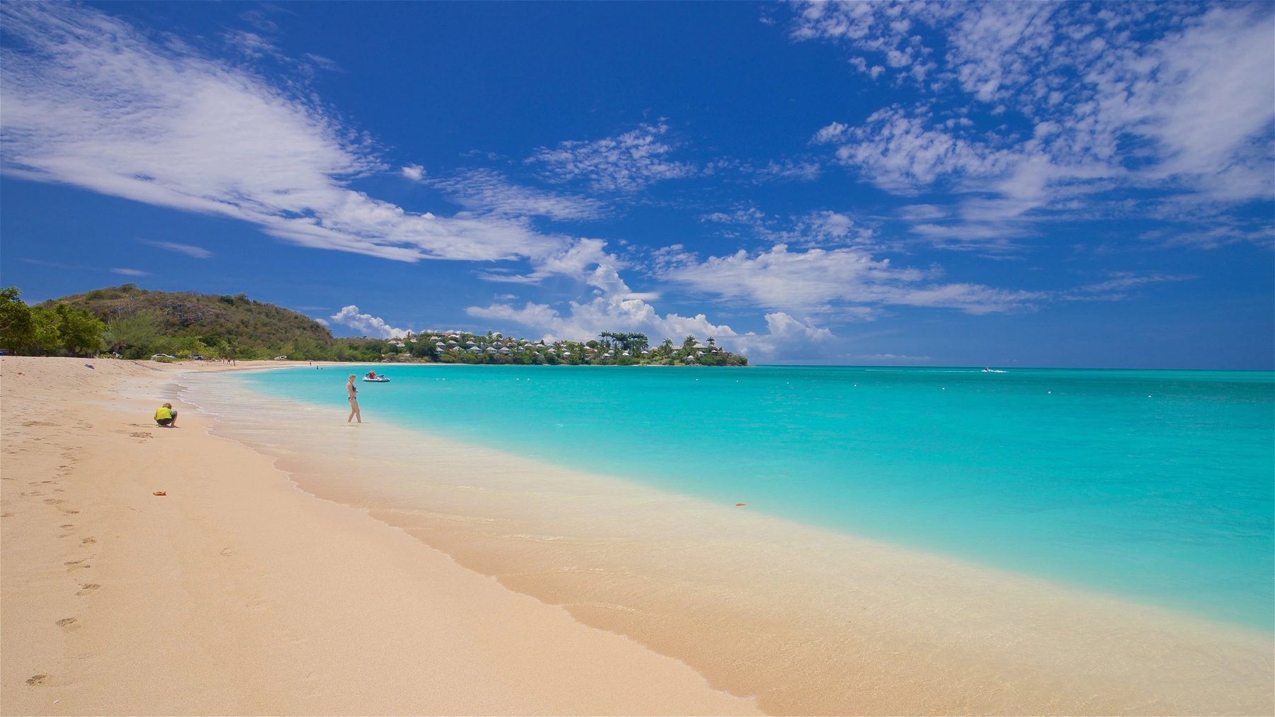 Long turquoise shoreline curving toward a green headland dotted with houses under a bright sky
