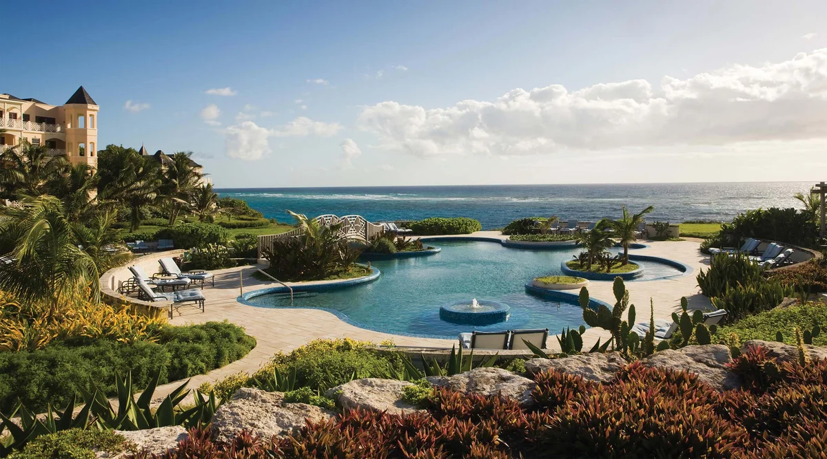 Resort pool complex at golden hour: free-form pool with a central fountain and planted island, stone