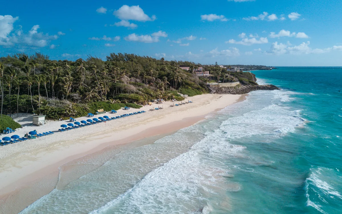 Drone photo of Crane Beach: rows of blue loungers and umbrellas along pale sand, turquoise surf breaking across