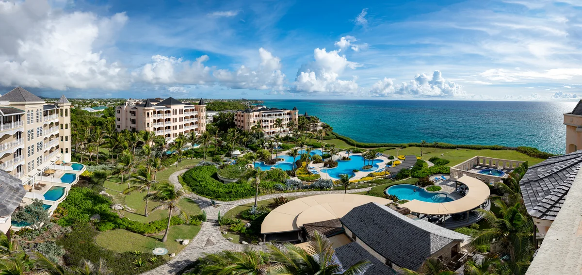 Very wide stitched panorama over the resort from an upper balcony: coral-stone residence buildings left, the