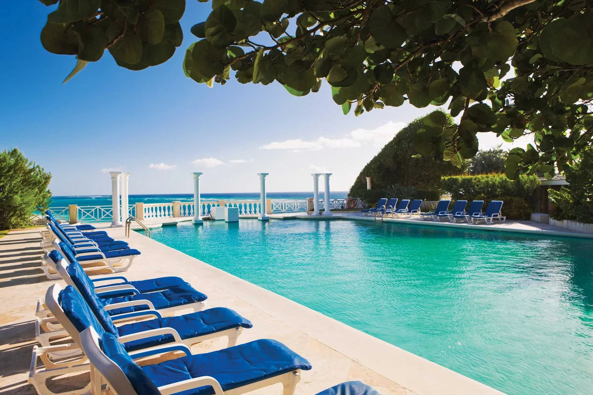 The historic long rectangular pool lined with blue-cushioned loungers, white classical columns and balustrade