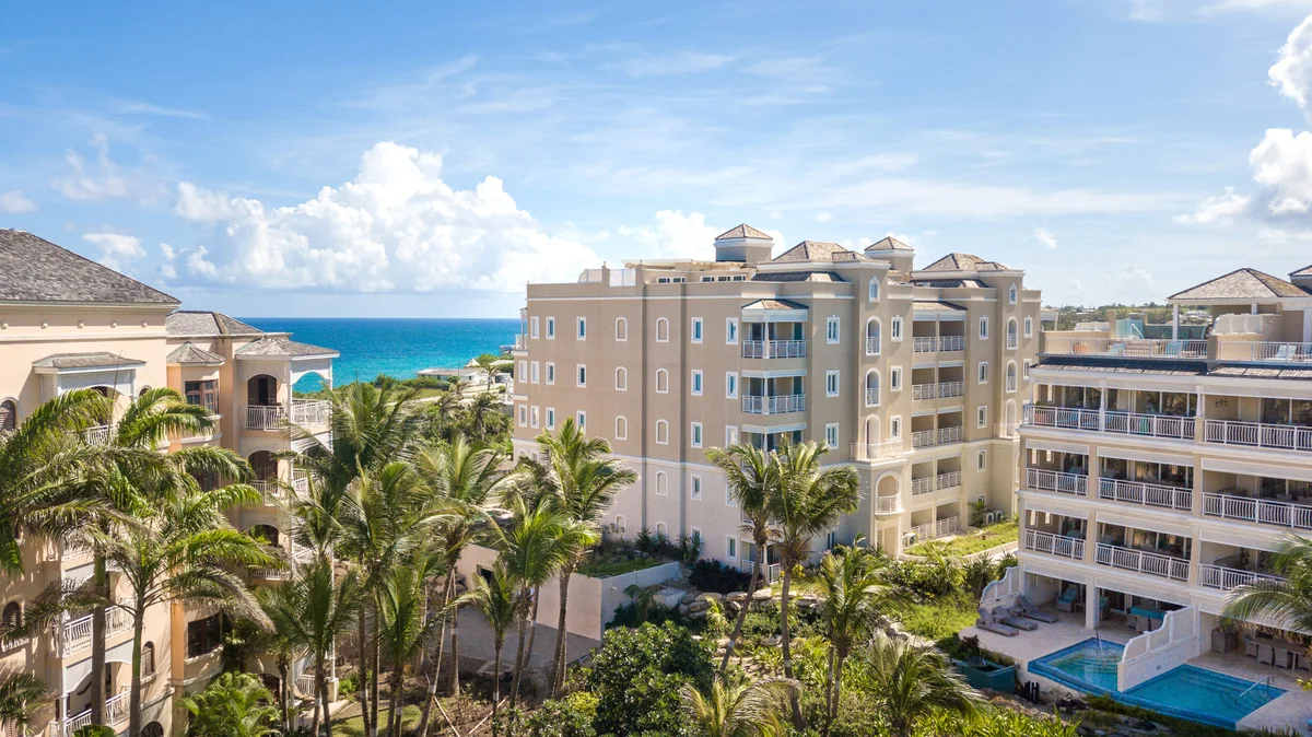 Drone photo at building height: cream and coral residence blocks with balconies and hipped roofs among mature