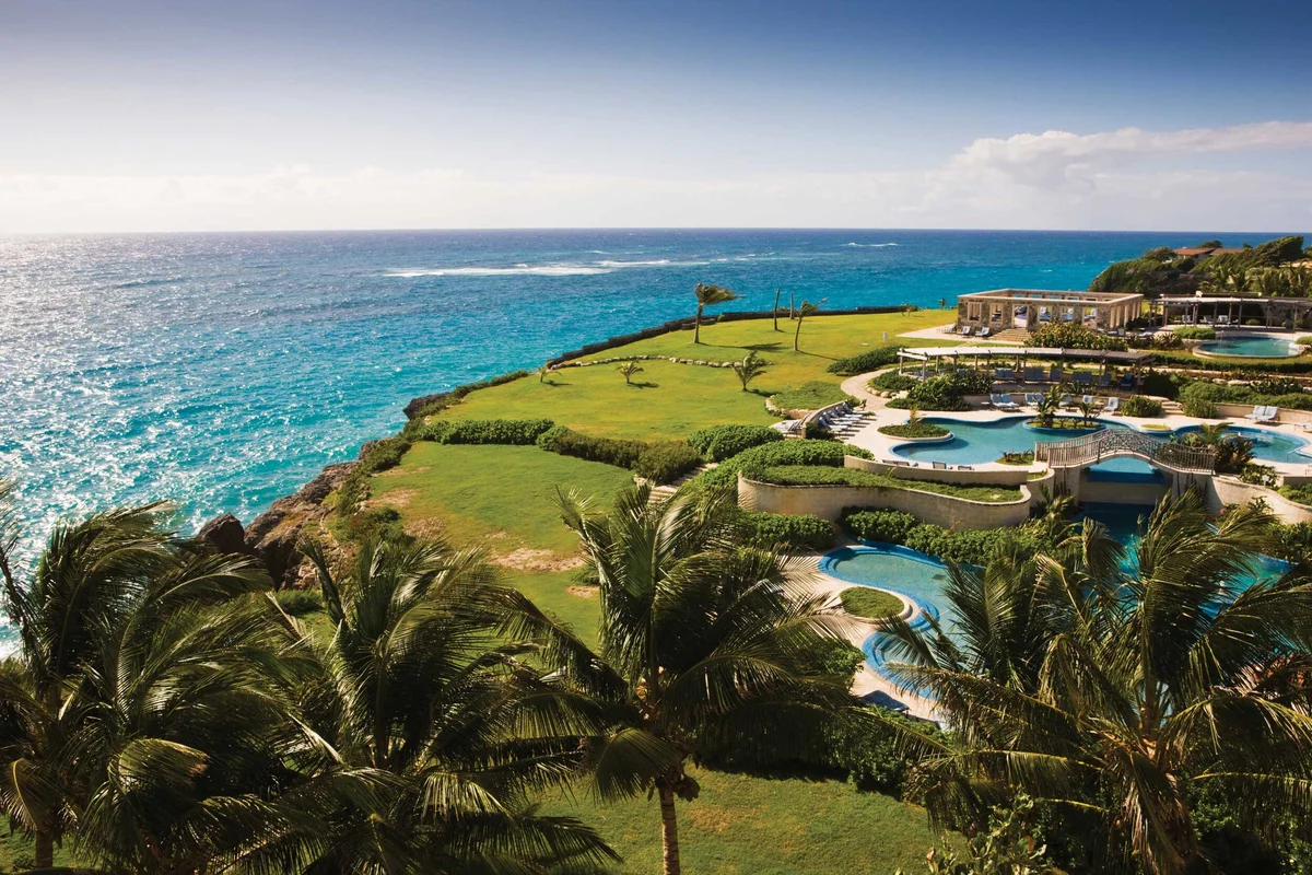 Elevated photo over the resort pool complex and clifftop lawn: terraced free-form pools with a stone