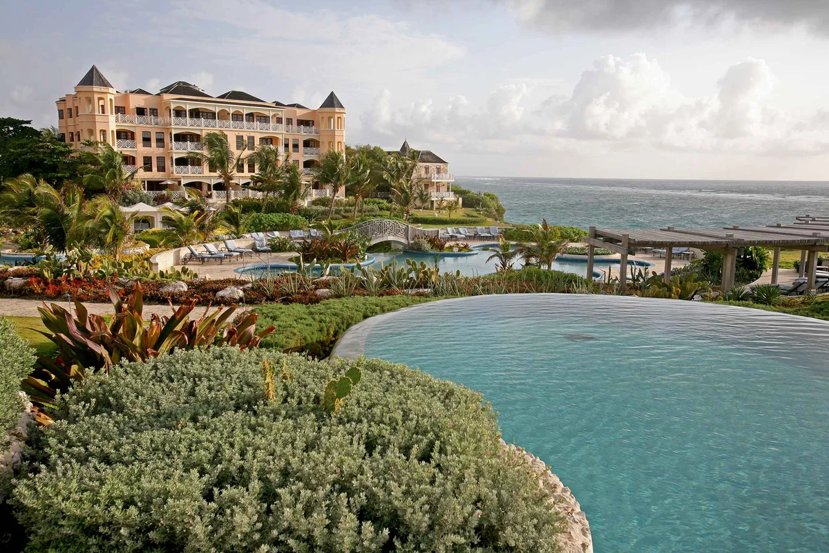 Resort pool photo: curved infinity edge in the foreground with silver-leaf planting, the coral-stone main