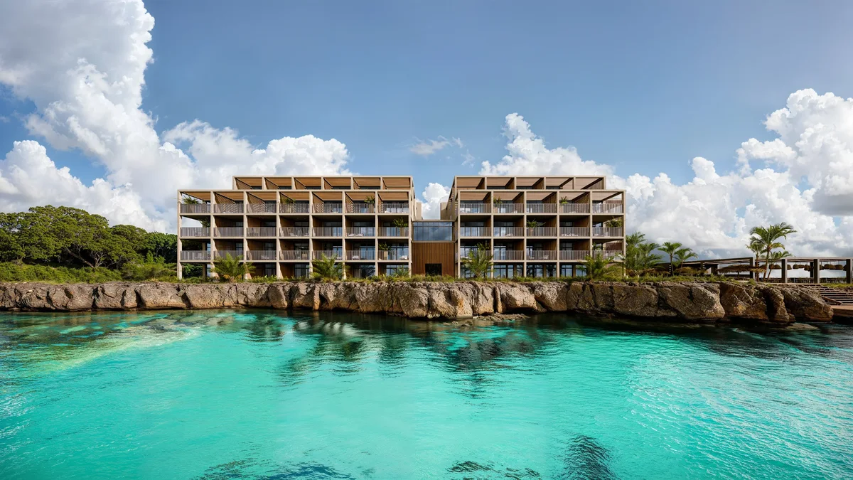 Artist’s rendering of head-on elevation seen from the water — two wings above a rocky shoreline, turquoise sea in the foreground.