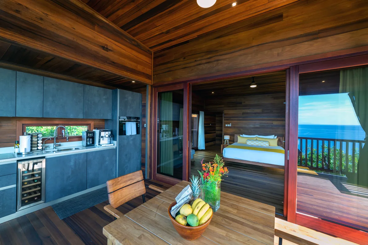 PHOTO β outdoor kitchen counter with wine fridge and coffee machine, fruit bowl on the dining table, bed