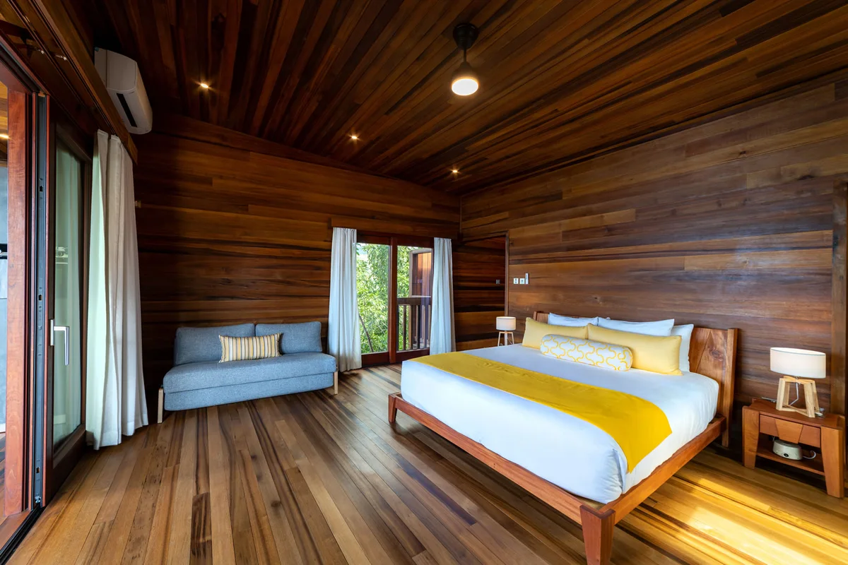 PHOTO β bedroom with timber walls, ceiling and floor, king bed with yellow runner, daybed under the window.