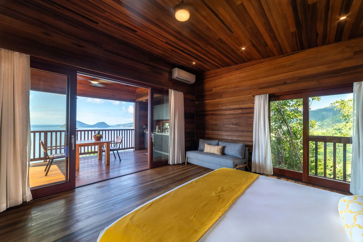 PHOTO β bedroom looking out through open sliding doors to the deck and sea; bed with yellow runner in the