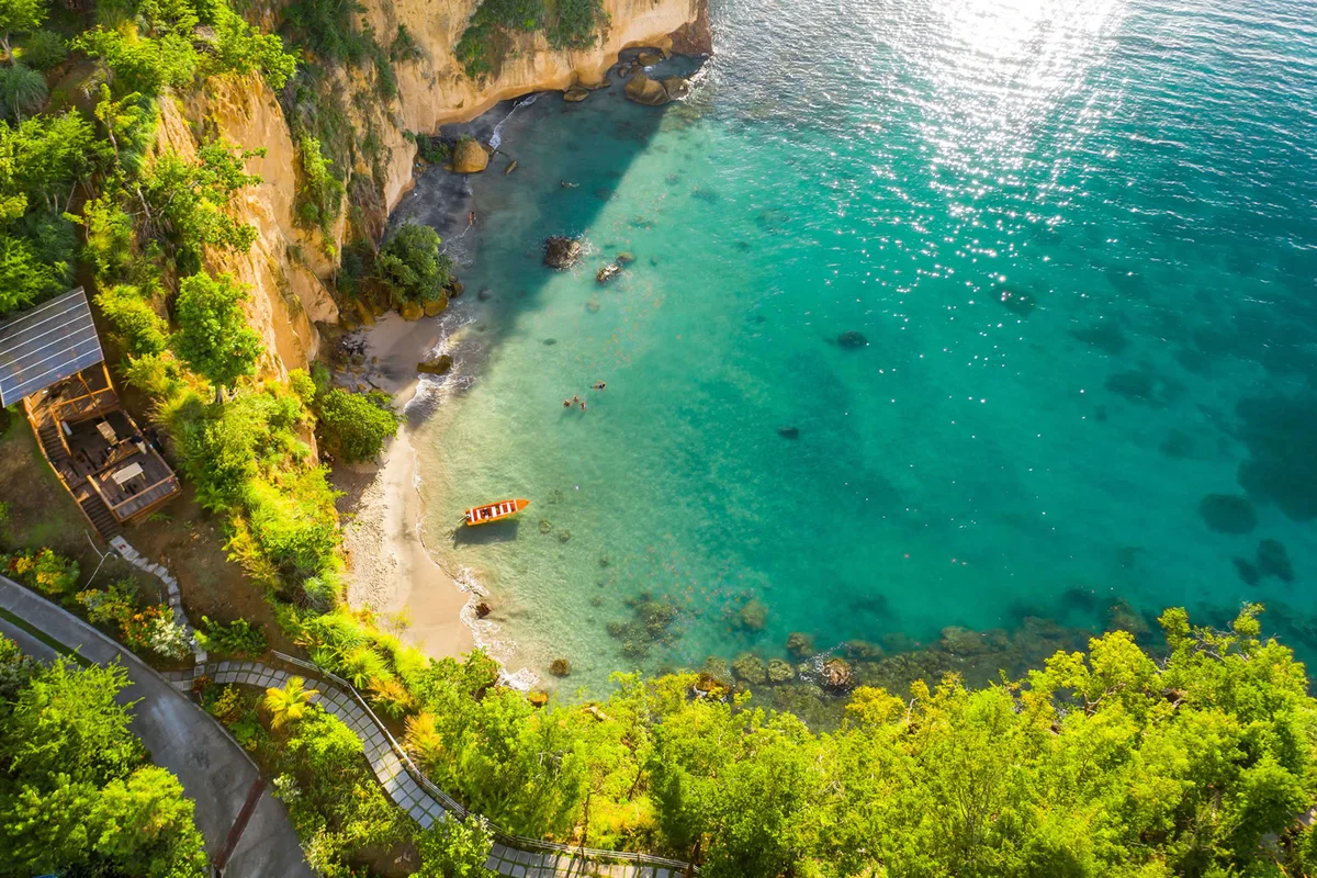 PHOTO β aerial over the resort's beach cove, cliff face, turquoise shallows with a red kayak. 1600x1066