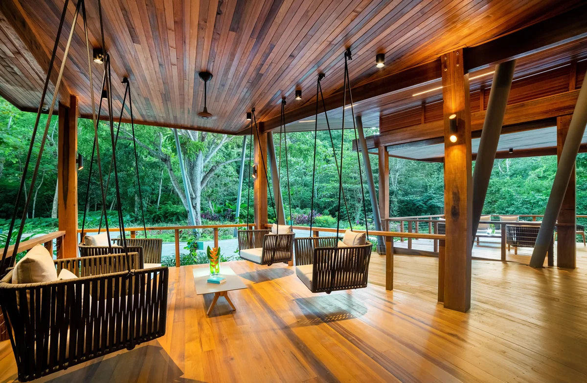 PHOTO β interior of an open-sided timber pavilion with hanging rattan swing seats and a polished timber floor,