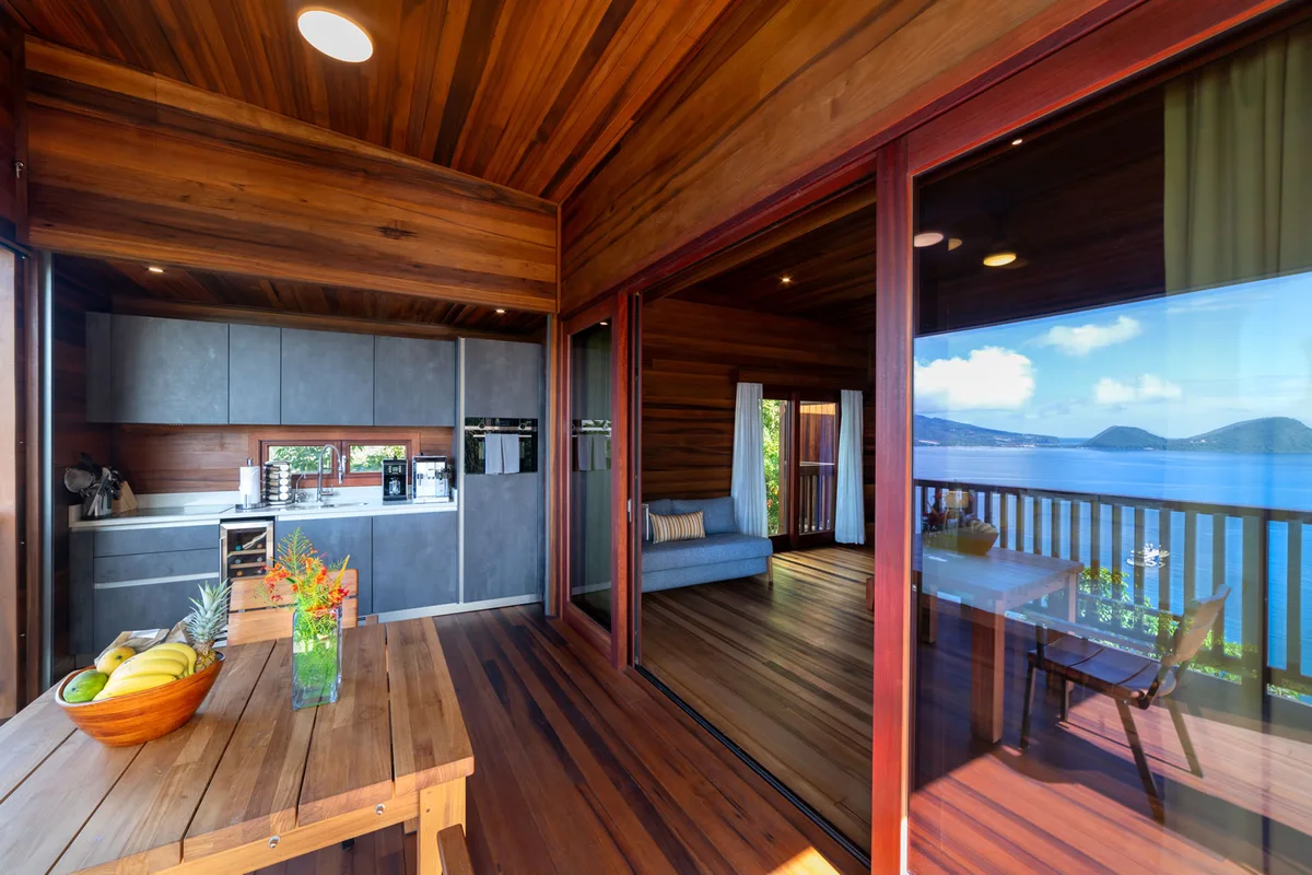 PHOTO β open-air kitchen with dark slab cabinetry alongside the timber dining deck, fruit and flowers on the
